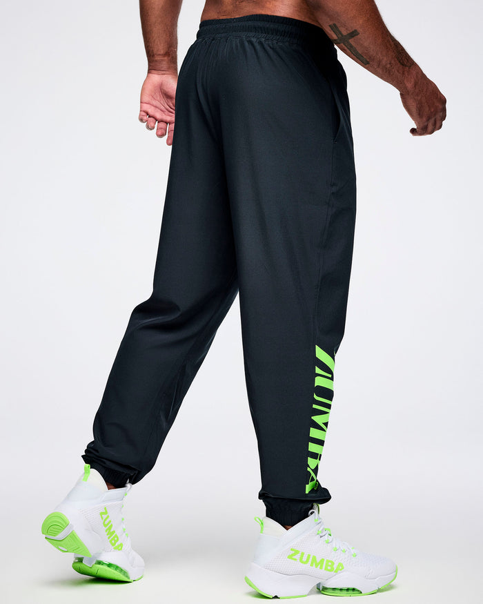 Back view of a male model wearing black cargo pants with green "ZUMBA" text on the right leg paired with white and green shoes.