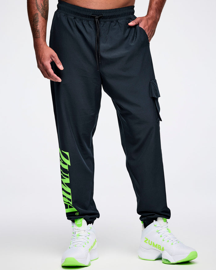 Front view of a male model with his left hand in the pocket of black cargo pants featuring green “ZUMBA” text on the right leg, paired with green-and-white shoes.