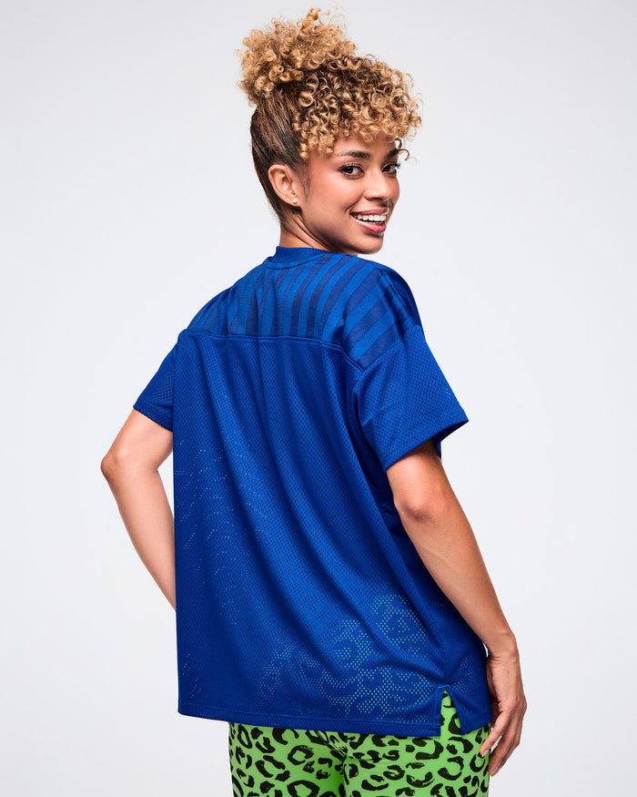 Back view of a female model wearing a blue Zumba mesh jersey, paired with matching green biker shorts.