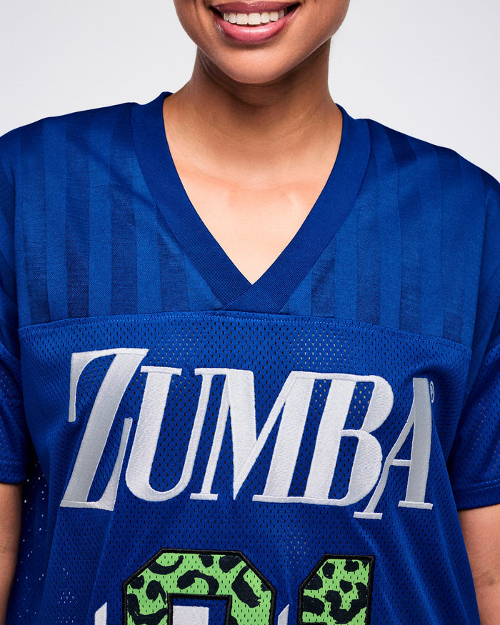 Close-up view of a female model wearing a blue Zumba mesh jersey with white “ZUMBA” text and patterned blue stripes on the shoulders.