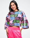 Female model wearing a colorful Zumba boxy crop top and pink pants on a white background.