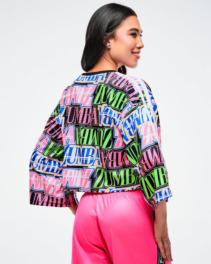 Back view of a female model wearing a colorful Zumba boxy crop top and pink pants on a white background.