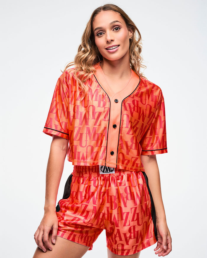Female model wearing an orange baseball top with red "ZUMBA" patterned text paired with matching boxer shorts on a white background.