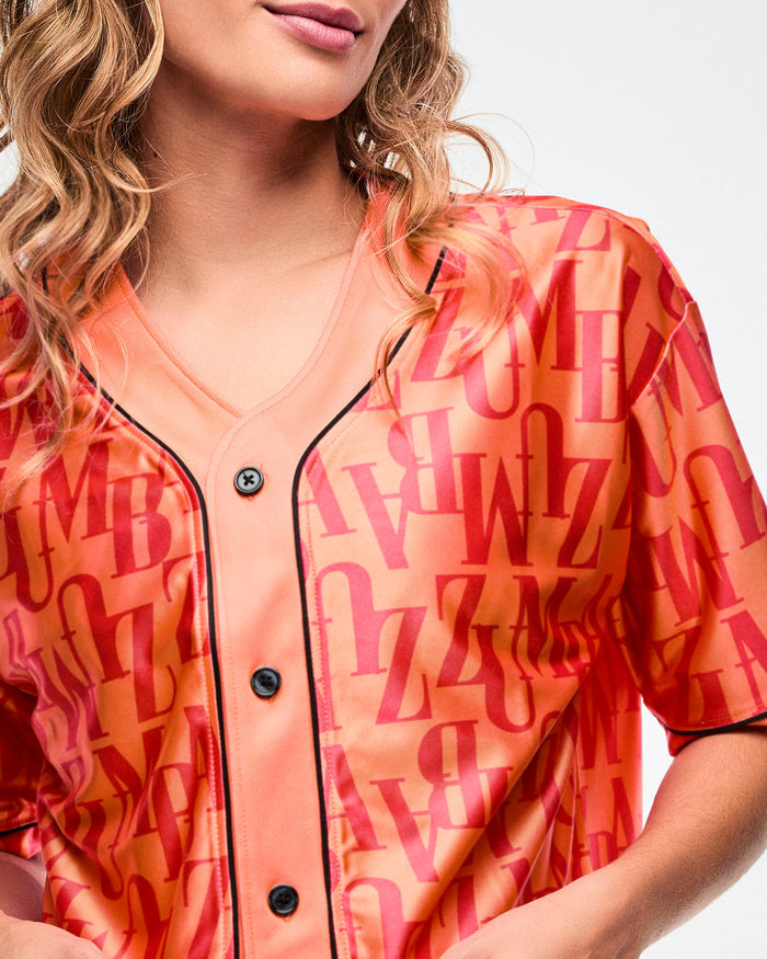 Close-up, detailed shot of the orange baseball top, highlighting its black buttons and trim, with bold red “ZUMBA” text across the fabric.