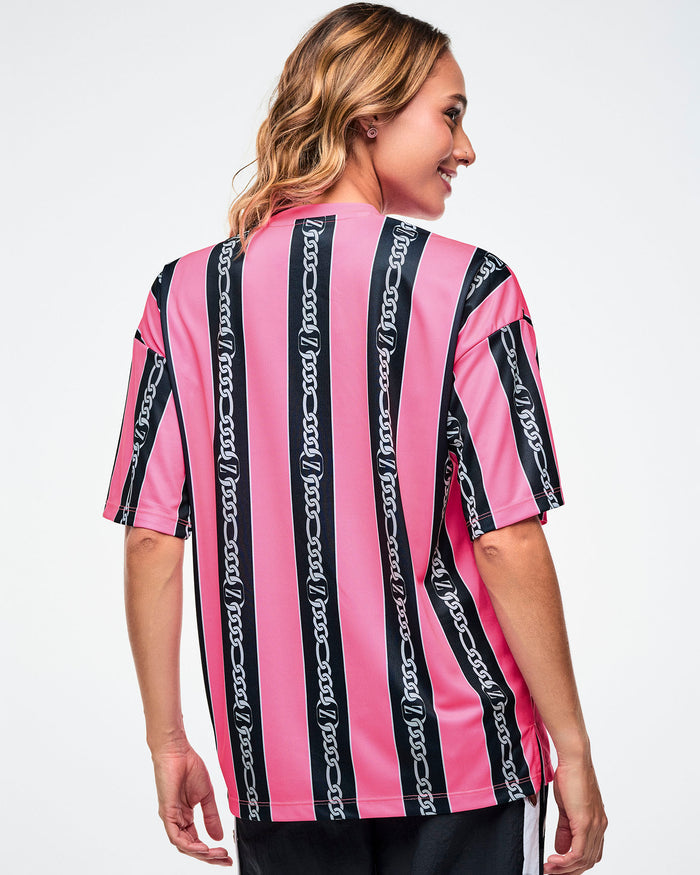 Back view of a female model wearing a pink-and-black striped Zumba top paired with black and white striped track pants on a white background.