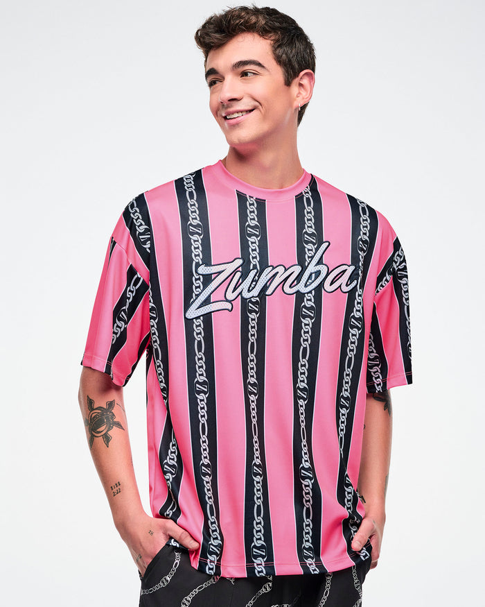 Male model wearing a pink-and-black striped Zumba top with white cursive “Zumba,” with black pants.