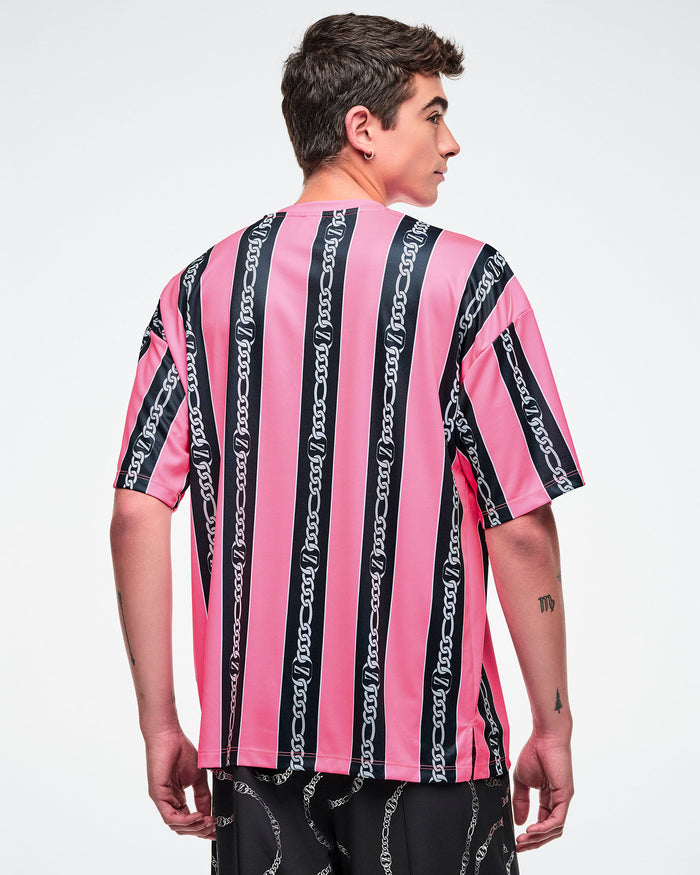 Back view of a male model wearing a pink-and-black striped Zumba top with white cursive “Zumba,” with black pants.