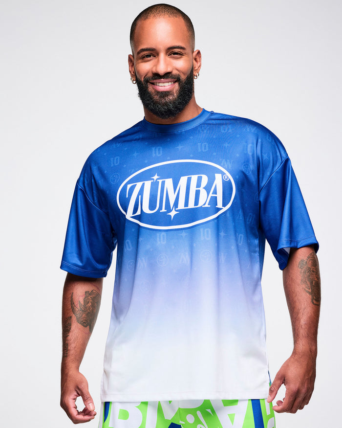 Male model wearing a blue-to-white gradient Zumba tee paired with blue and green patterned Zumba pants.
