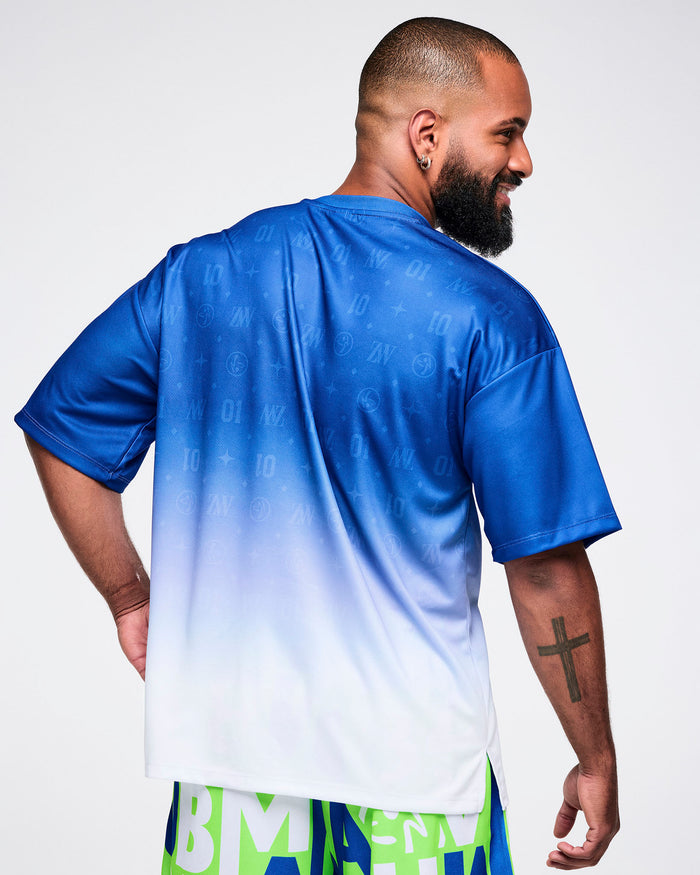 Back view of a male model wearing a blue-to-white gradient Zumba tee paired with blue and green patterned Zumba pants.