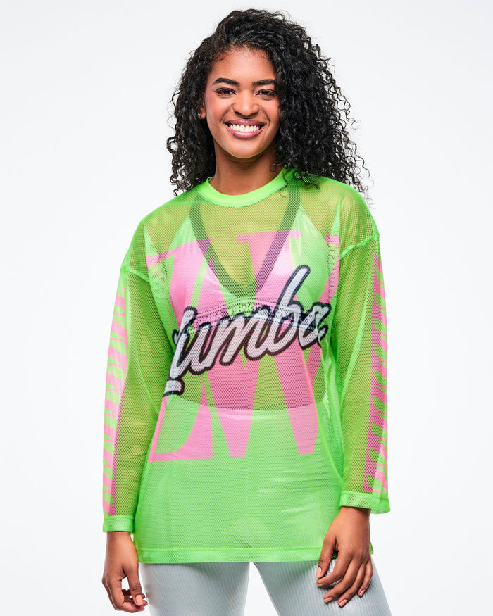 Female model wearing a neon green mesh Zumba top with a large pink “ZW” graphic and white cursive “Zumba” across the chest, paired with silver biker shorts.