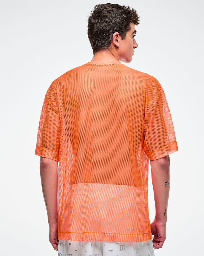 Back view of a male model wearing an oversized orange mesh Zumba top with bold vertical “ZUMBA” silver lettering paired with white and silver pants.