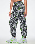 Female model wearing black and white patterned ZUMBA pants with green Zumbito accents, paired with white and green sneakers on a white background.