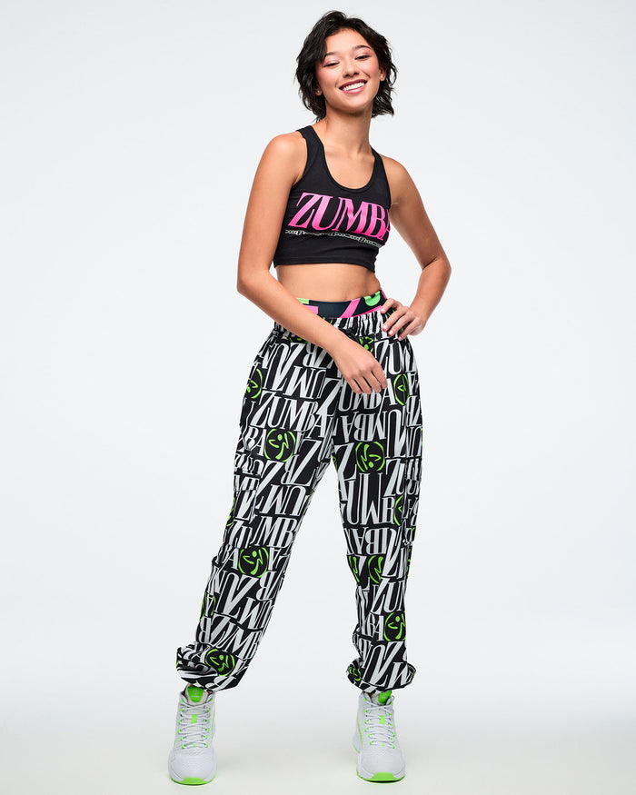 Female model wearing a Zumba branded top and black and white pants with green Zumbito accents on a white background.