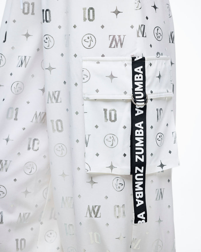 Close-up of the cargo pocket with a black‑and‑white “Zumba” ribbon, set against the silver Zumba motif print.