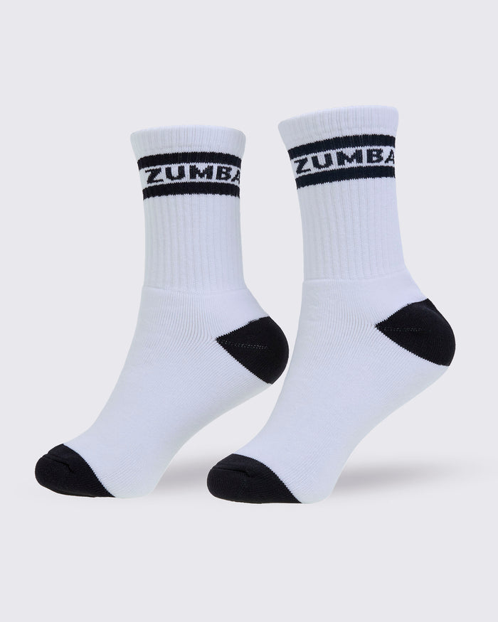 A pair of white crew socks with black accents, featuring the brand name 'ZUMBA' printed in white on a black band around the ribbed ankle cuffs, set against a light gray background.