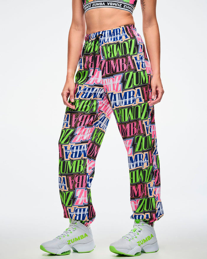 Female model wearing colorful Zumba pants paired with green and white shoes on a white background.