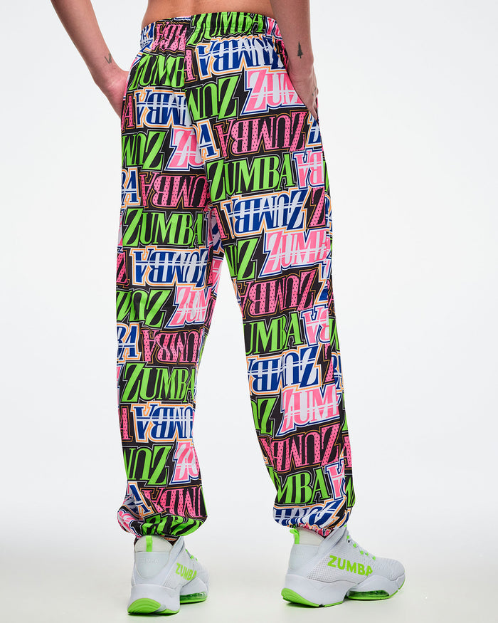 Back view of a male model wearing multicolored woven pants paired with white and green shoes.