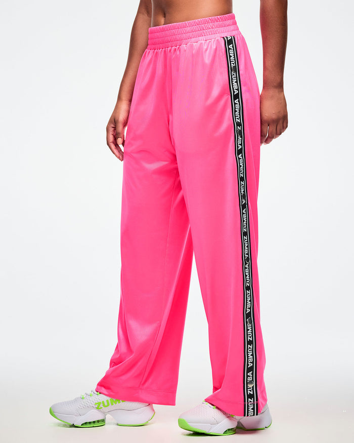 Female model wearing pink track pants with a black and white Zumba side stripe on a white background.