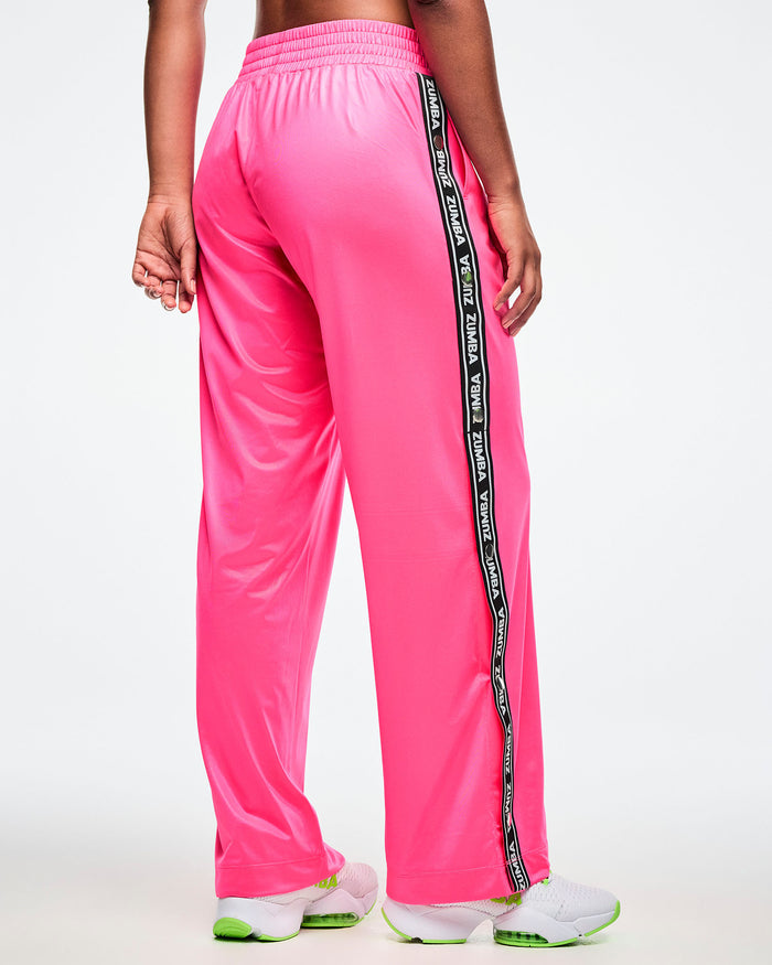 Back view of a female model wearing pink track pants with a black and white Zumba side stripe on a white background.