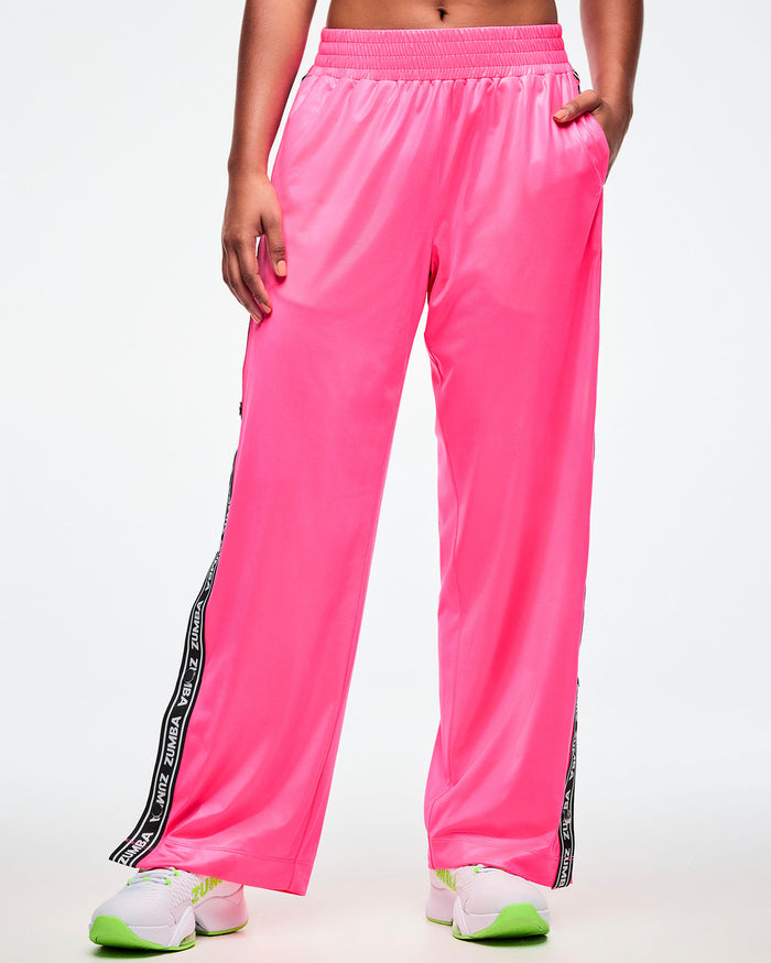 Front view of a female model wearing pink track pants with her left hand in her pocket on a white background.
