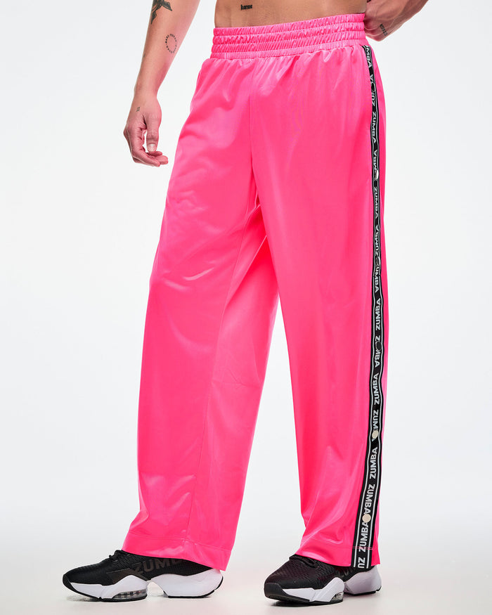 Male model wearing pink track pants with a black and white Zumba side stripe on a white background.