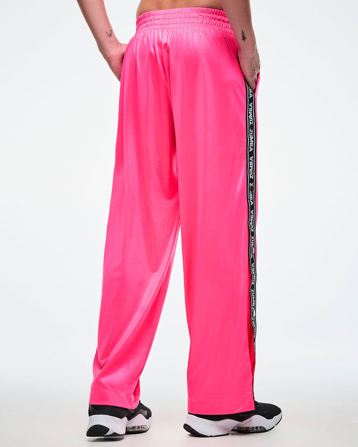 Back view of a male model wearing pink track pants with a black and white Zumba side stripe on a white background.