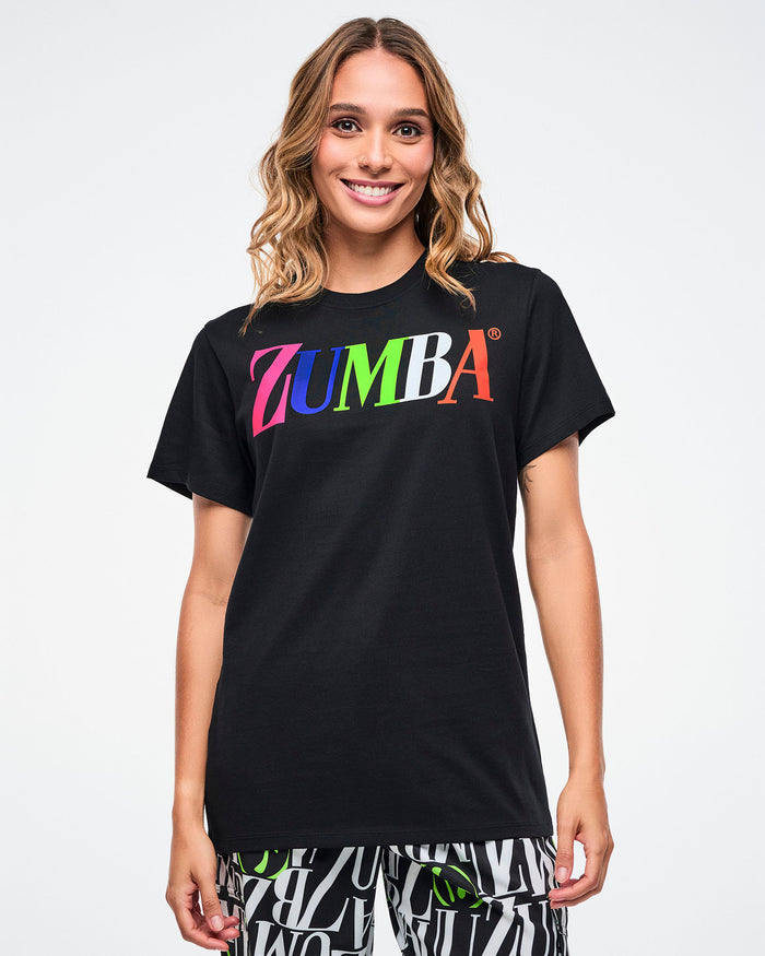 Female model wearing a black Zumba tee with colorful “ZUMBA” text across the chest on a white background.