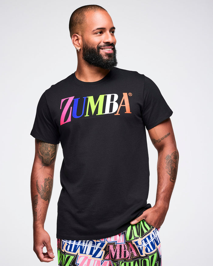 Male model wearing a black Zumba tee with colorful “ZUMBA” text across the chest, paired with multicolored pants on a white background.
