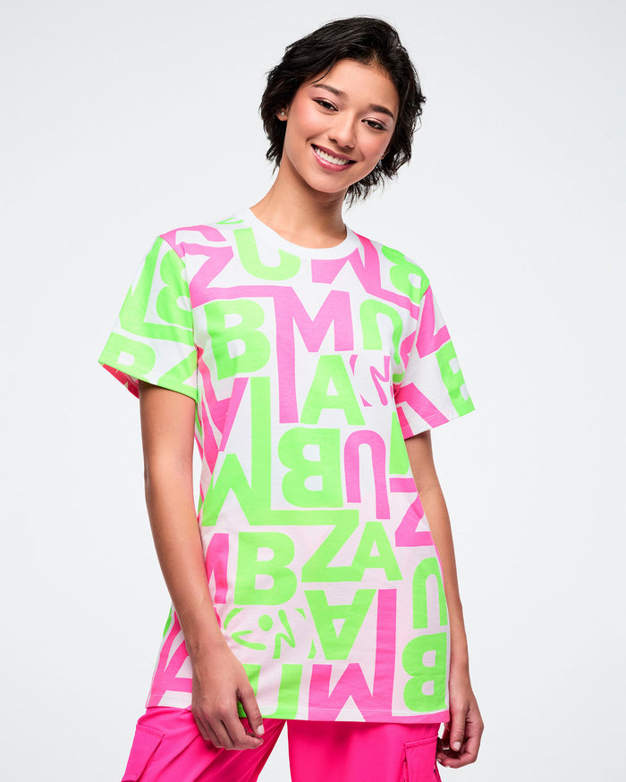 Female model wearing a bright neon green and pink patterned white tee paired with pink pants.