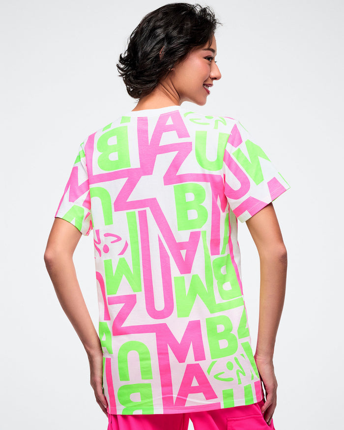 Back view of a female model wearing a bright neon green and pink patterned white tee paired with pink pants.