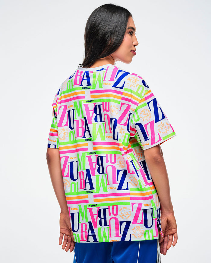 Back view of a female model wearing a colorful Zumba t-shirt on a white background.