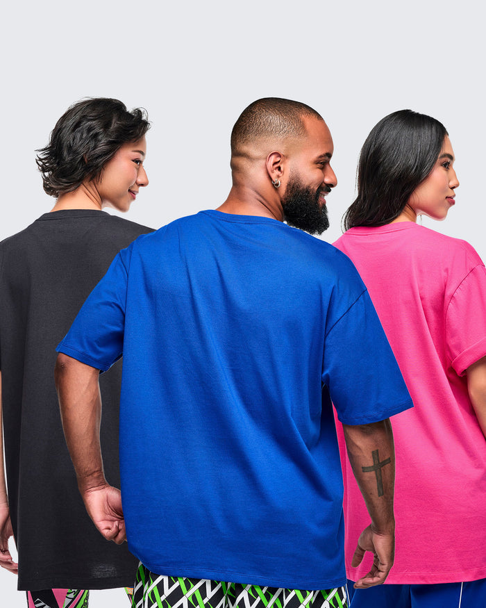 Back view of three models wearing Zumba branded t-shirts in black, blue and pink on a plain background.
