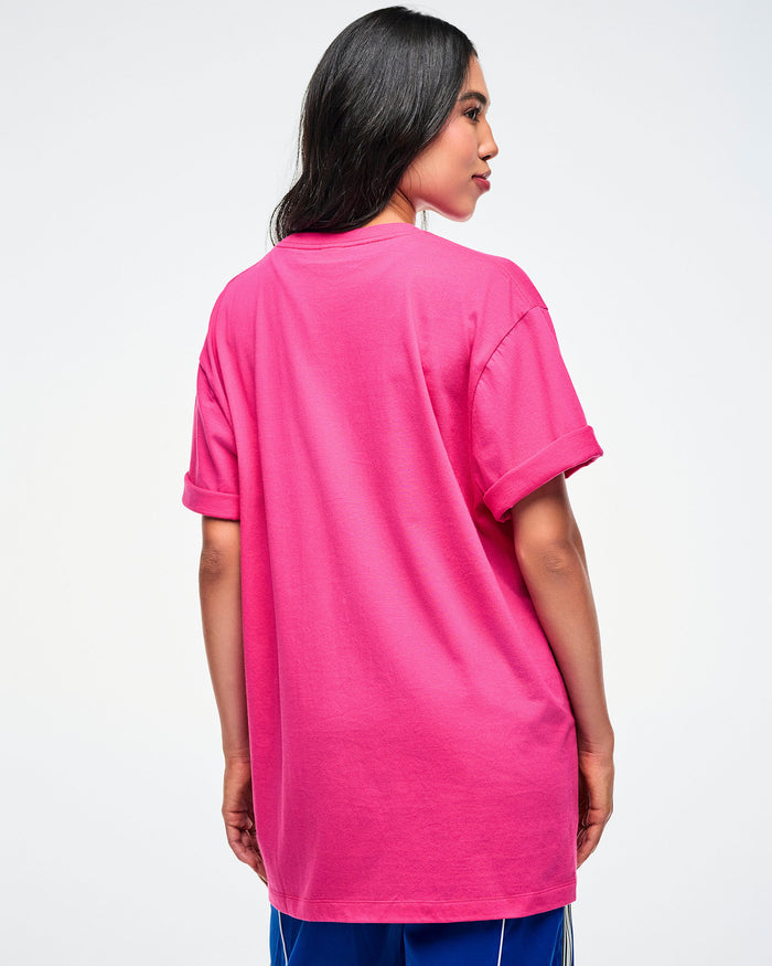 Back view of a female model wearing a pink Zumba shirt with colorful text on a white background.