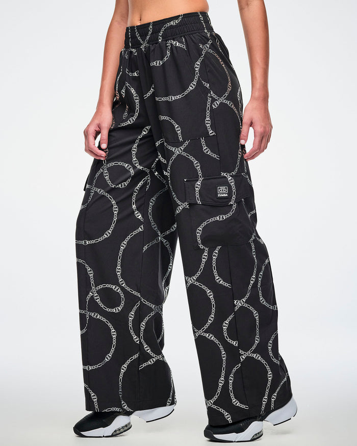Black cargo pants with silver chain pattern worn by a female model and paired with black and white shoes.