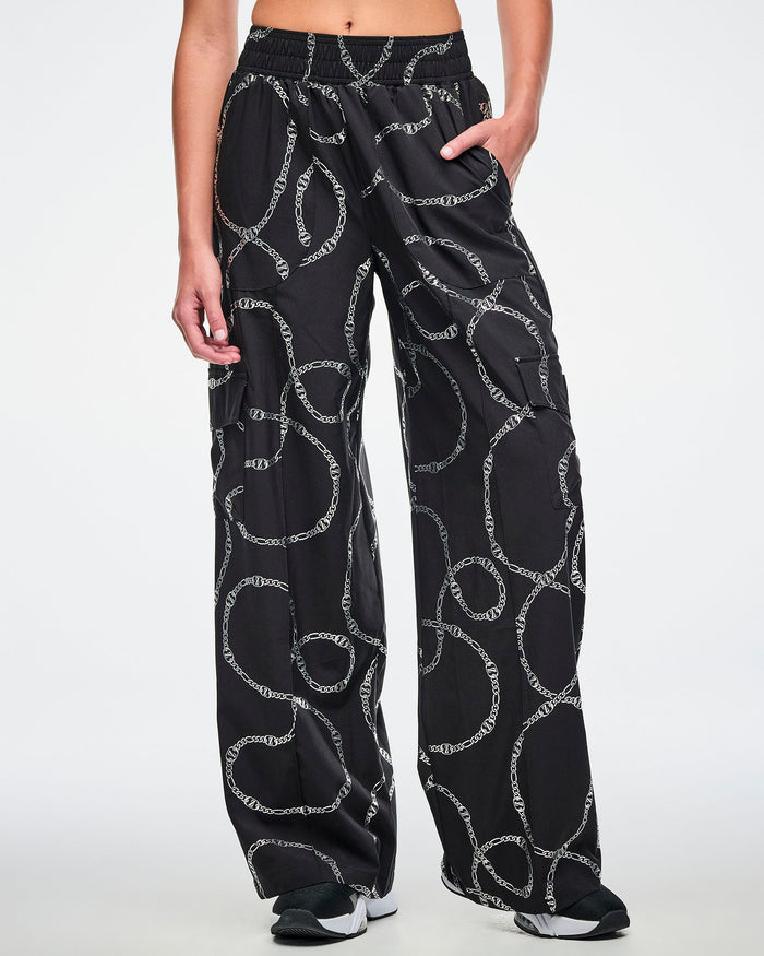Female model with hand in the left pocket of the black cargo pants with silver chain pattern and paired with black and white shoes.