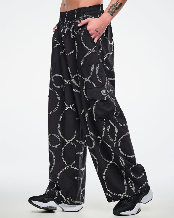 Male model wearing black cargo pants with silver chain pattern, paired with black and white shoes.