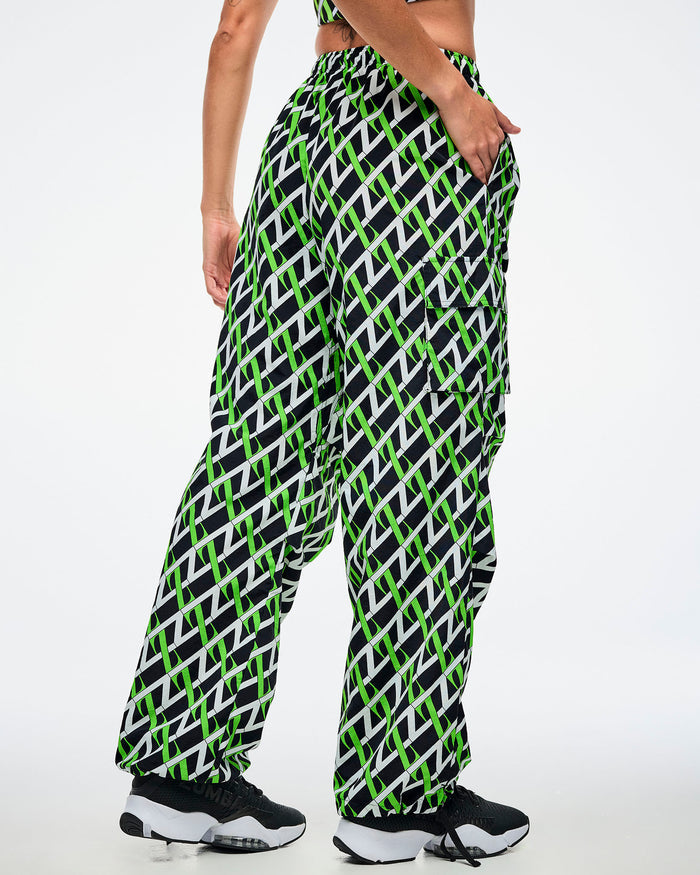 Back view of a female model wearing cargo pants with an allover black, white and green “Z” crisscross pattern, left hand in her pocket, paired with black-and-white shoes.