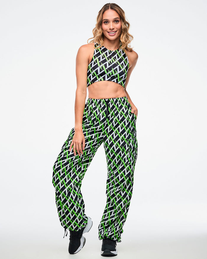 Female model wearing cargo pants with an allover black, white and neon green “Z” crisscross pattern, left hand in her pocket, paired with matching crop top and black-and-white shoes.