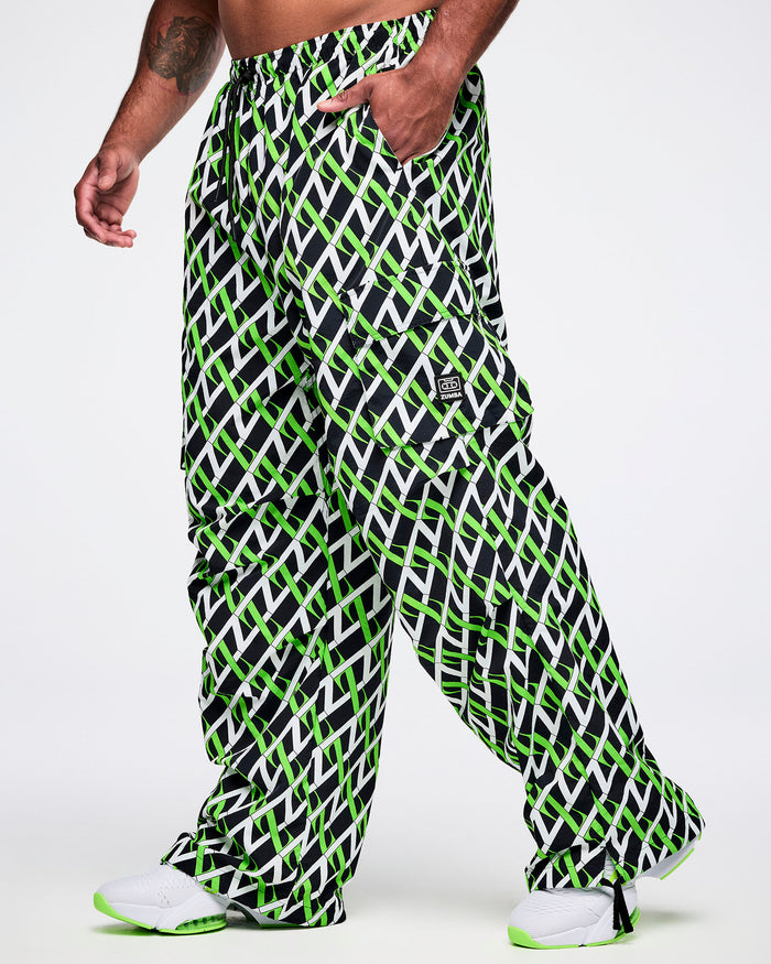 Male model wearing black cargo pants with an allover black, white and green “Z” crisscross pattern, left hand in his pocket, paired with black-and-white shoes.