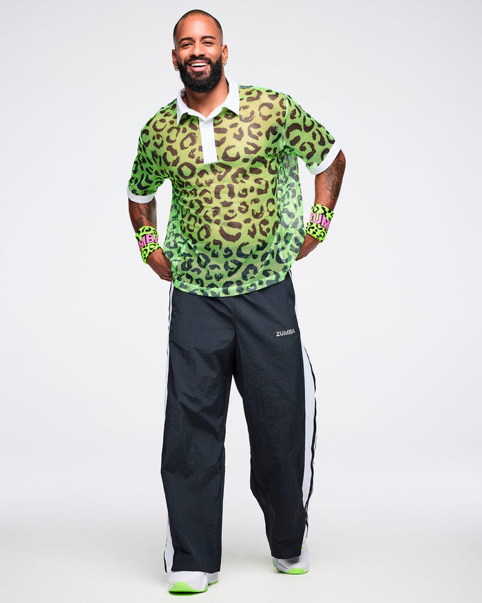 Male model wearing a green leopard print wristbands with ZUMBA in pink text, paired with a matching polo shirt and black and white pants.