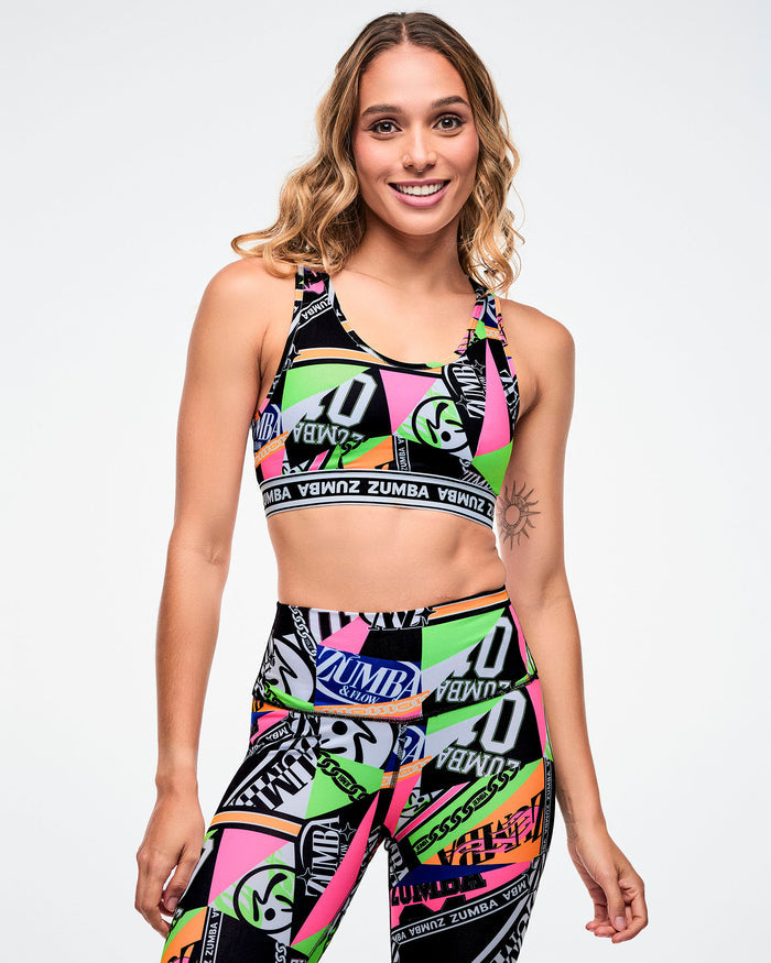 Female model wearing a colorful Zumba sports bra and matching leggings on a white background.