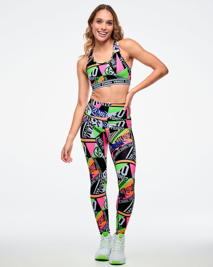 Female model wearing a colorful sports bra and leggings set with white and green shoes on a white background.