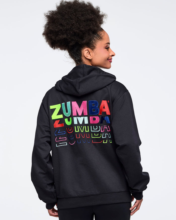 Female model wearing a black hoodie with colorful 'ZUMBA' text on the back against a white background