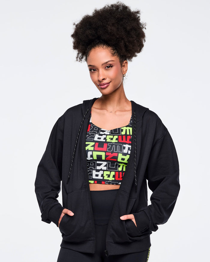 Female model wearing a black hoodie and colorful sports bra with multi color text on a white background.