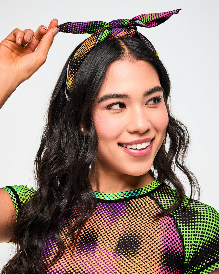 Female model wearing a bandana tied as a hair accessory and paired with a matching, colorful halftone mesh crop top.