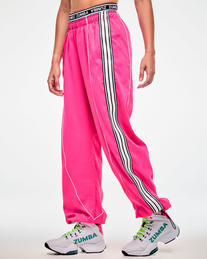 Female model wearing pink track pants with a white and black side stripe and white sneakers, side view.