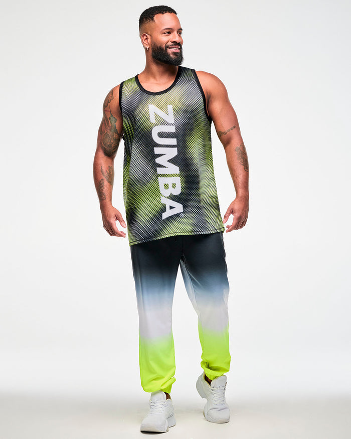 Full view of a male model wearing a black and yellow halftone dot-print tank top with white "ZUMBA" vertical text, ombre, black, white, yellow, joggers, and white sneakers.