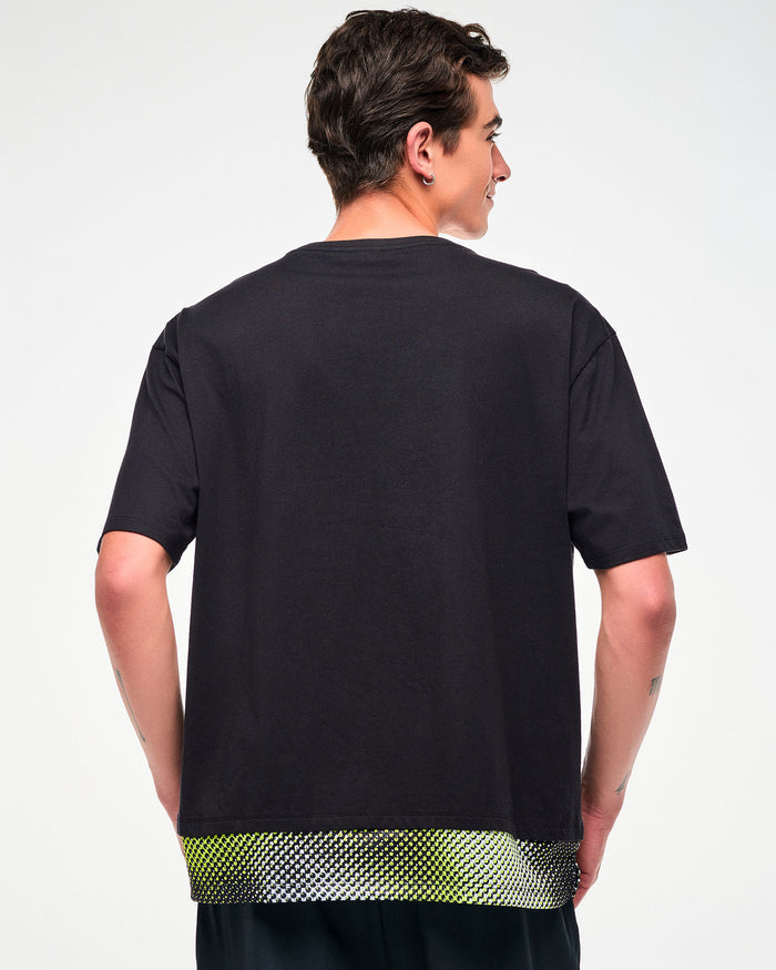Male model wearing a black oversized T-shirt with a yellow, black, and white mesh dot-print hem, shown from the back.