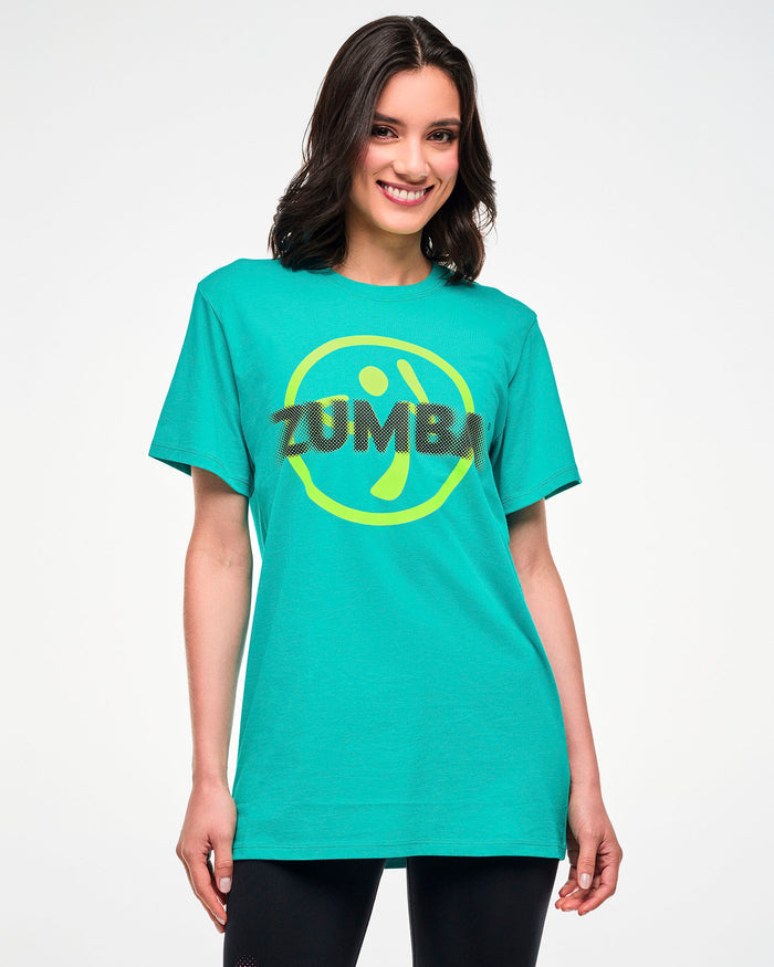 Female model wearing an aqua tee with a yellow Zumbito logo and halftone black dot "ZUMBA" text.