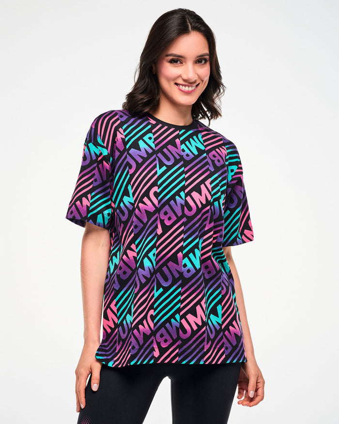 Female model wearing a black tee with a colorful pink, aqua, and purple diagonal striped "ZUMBA" broken patterned print.